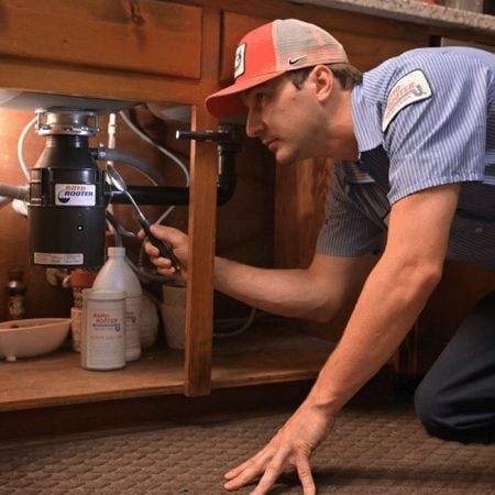 Plumber working on a garbage disposal beneath the sink.
